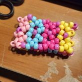 kandi cuff made out of pale pink, blue, yellow, and 
    magenta beads